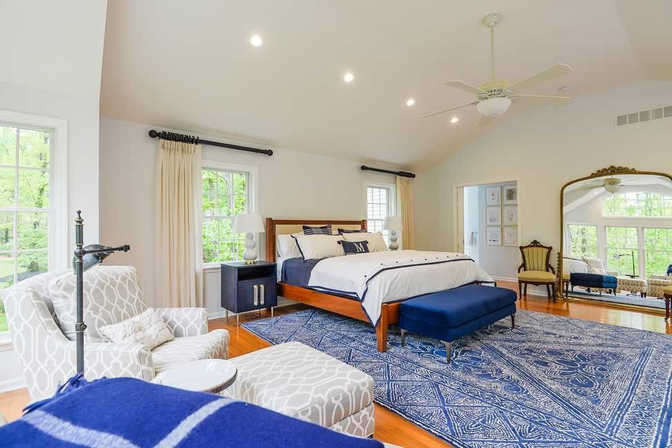 Spacious bedroom featuring a king bed with white bedding, navy accent bench, patterned rug, and a large arched mirror.