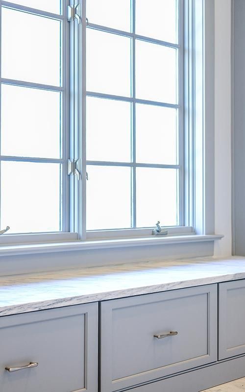 A light blue window seat with built-in drawers beneath a large, multi-pane white window.