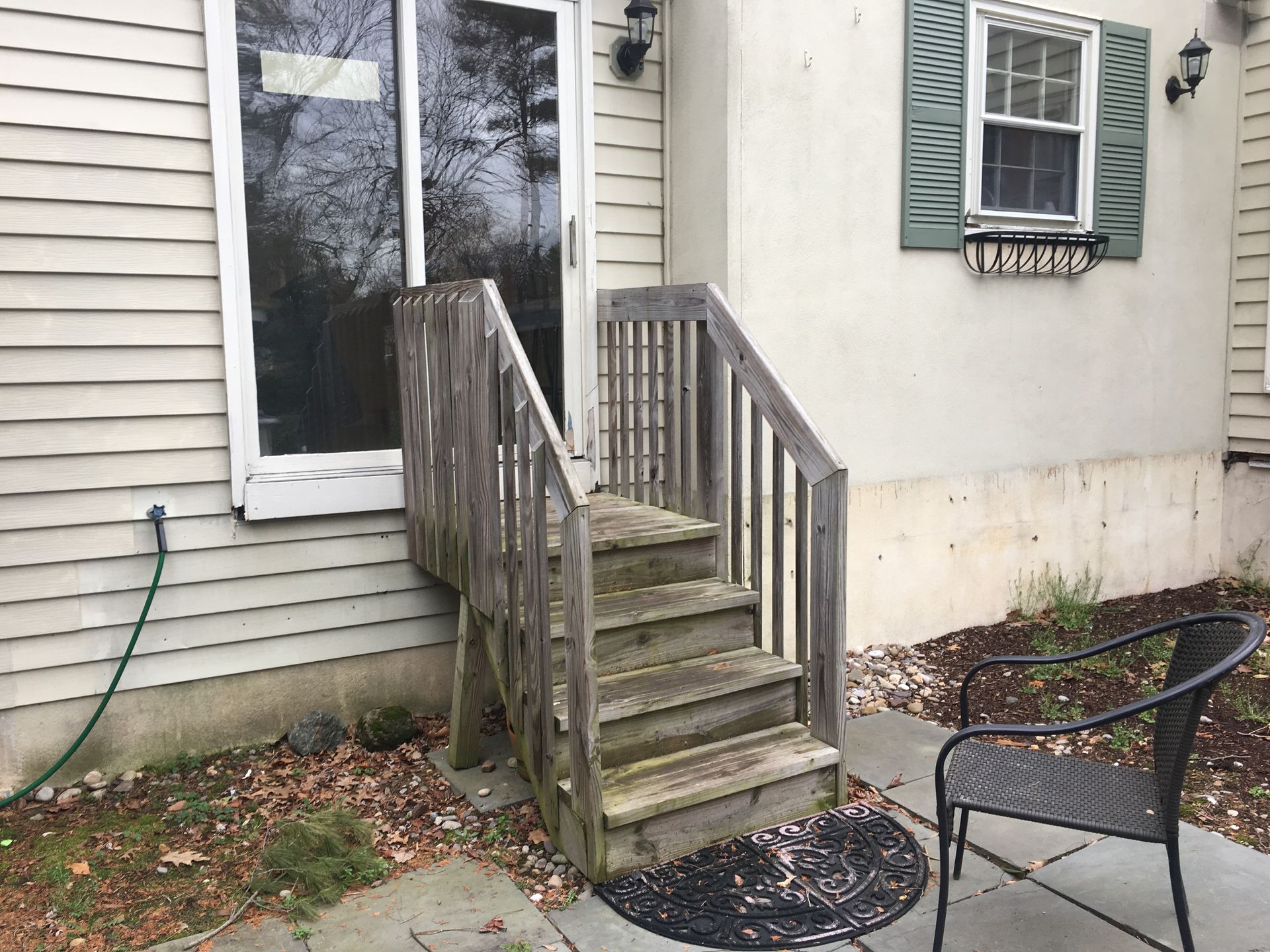 A set of weathered wooden steps with railings leading to a sliding glass door on the side of a light-colored house.