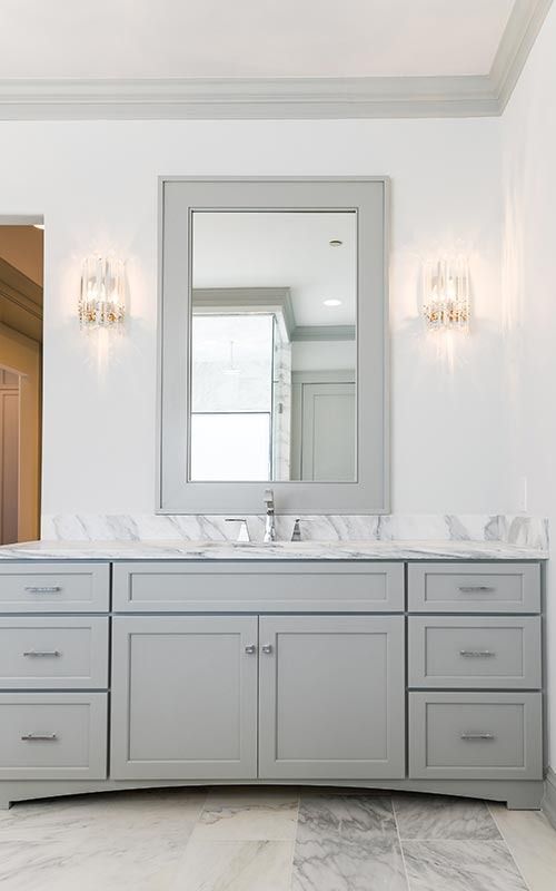 A modern bathroom vanity with a gray cabinet, marble countertop, large mirror, and two wall-mounted light fixtures.