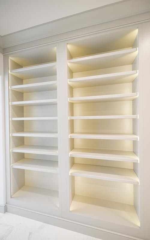 Two built-in, white shelving units with recessed lighting and matching wooden shelves.