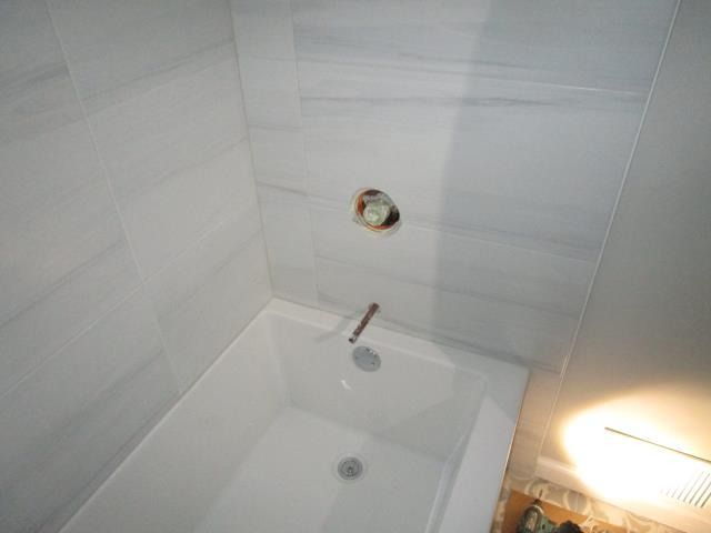 A white bathtub set against tiled walls with an exposed plumbing valve and spout pipe.