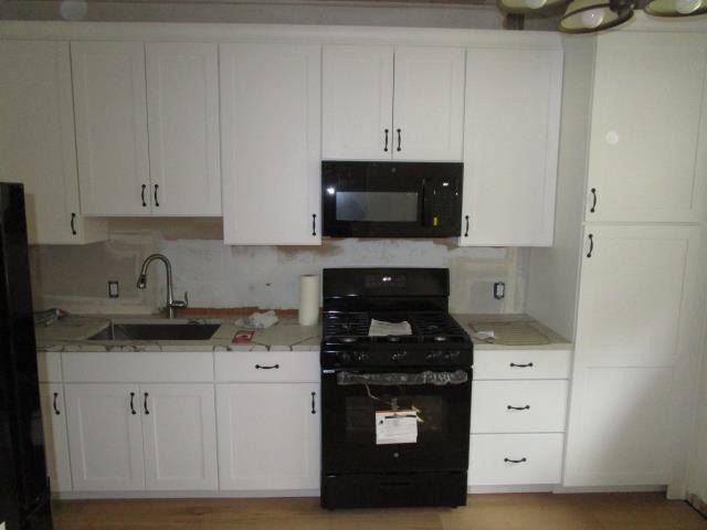 A kitchen with white cabinets, black appliances, a sink, and an unfinished backsplash.
