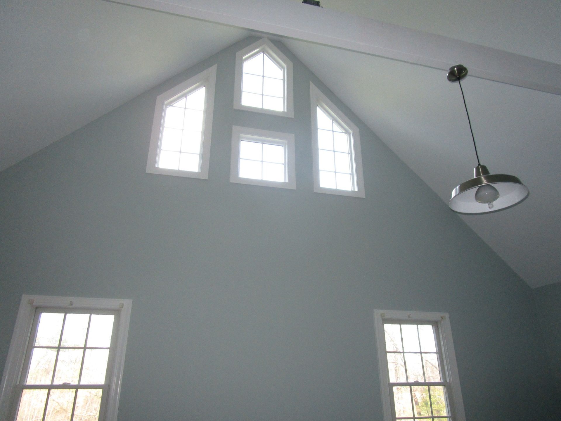 A light gray room with a vaulted ceiling featuring two lower windows and three upper windows, with a hanging pendant light.