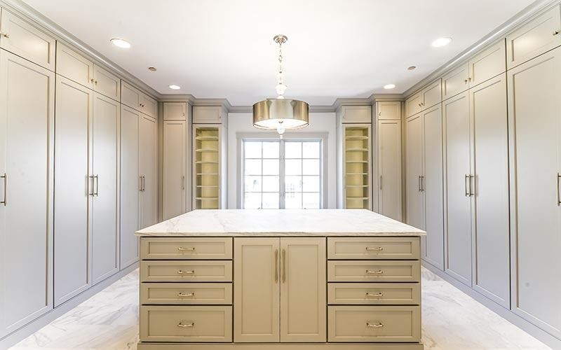 A luxurious, symmetrical walk-in closet with light gray cabinetry, marble floors, a central island, and a drum pendant.