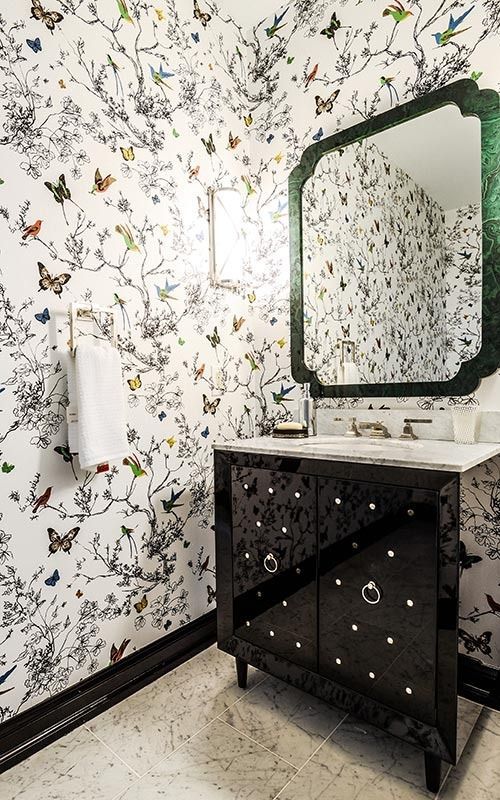 A bathroom with butterfly-patterned wallpaper, a black vanity with silver hardware, and a dark-framed wall mirror.