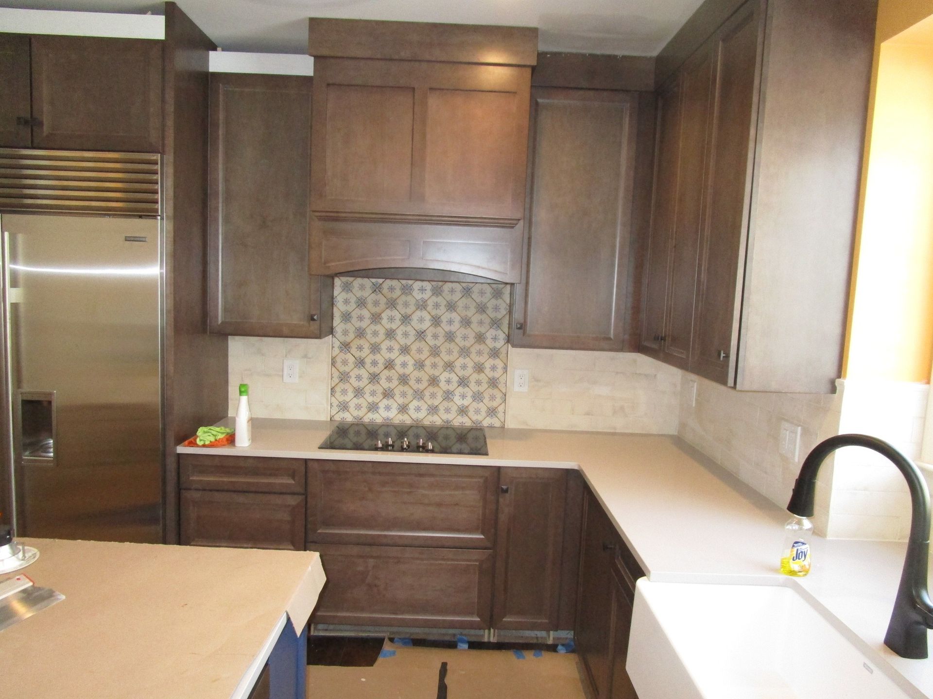 Dark brown kitchen cabinets, a stainless steel refrigerator, white countertops, and a patterned tiled stove backsplash.