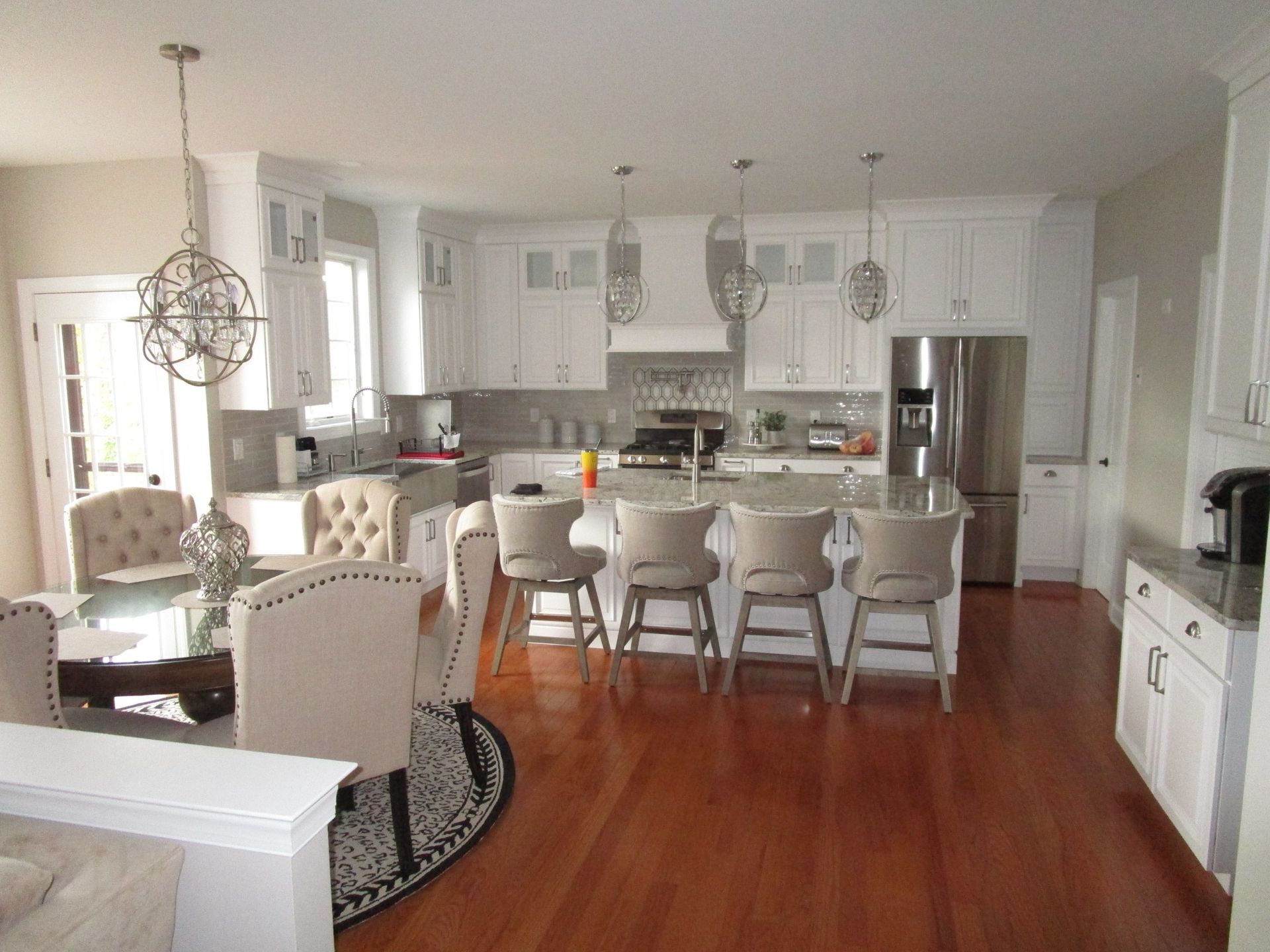 A bright, white kitchen with a wooden floor, central island, bar seating, and a dining area with a round table.