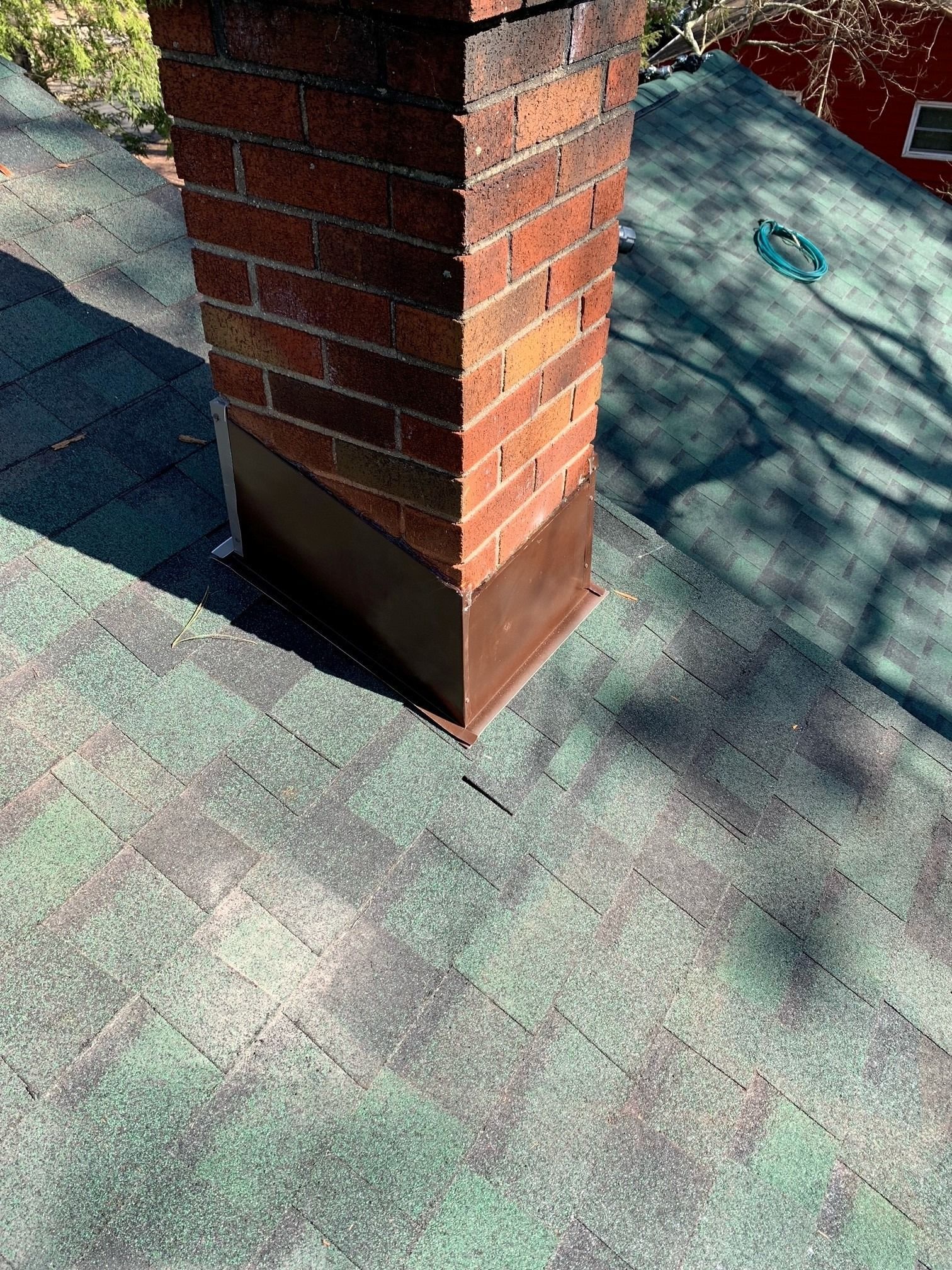 A brick chimney on a green shingled roof with copper flashing at the base.