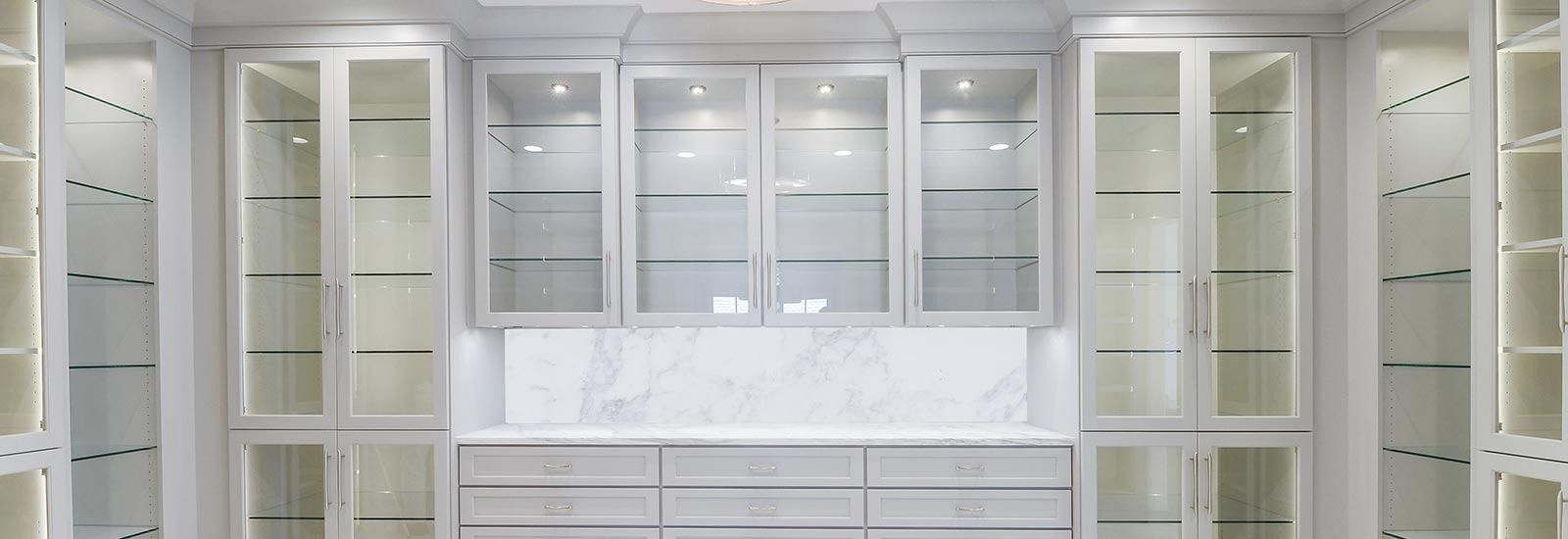 White closet storage with glass-front cabinets, internal lighting, and a marble countertop.
