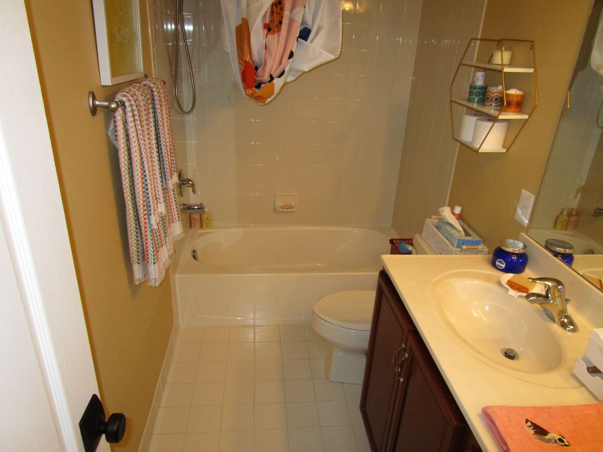 A bathroom featuring a beige bathtub with a shower, a white toilet, and a vanity with a white countertop and dark cabinets.