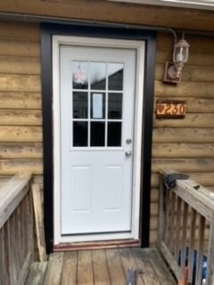White door with a window set in a log cabin frame, featuring dark trim and a house number sign reading 230 on the wall.