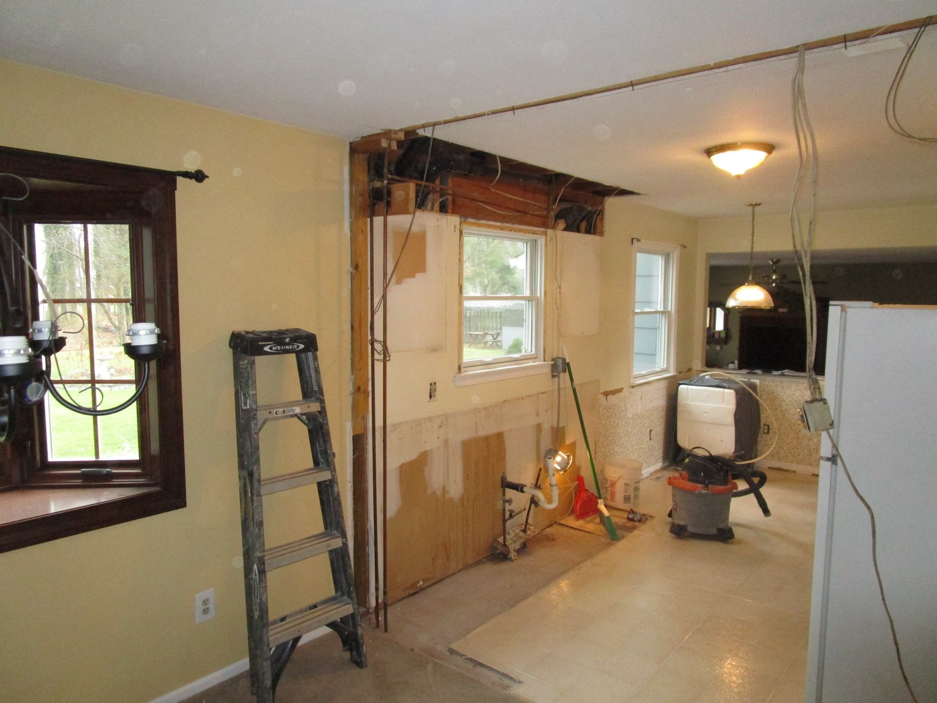 A residential room undergoing interior renovation with exposed wall framing, a step ladder, and a shop vacuum.