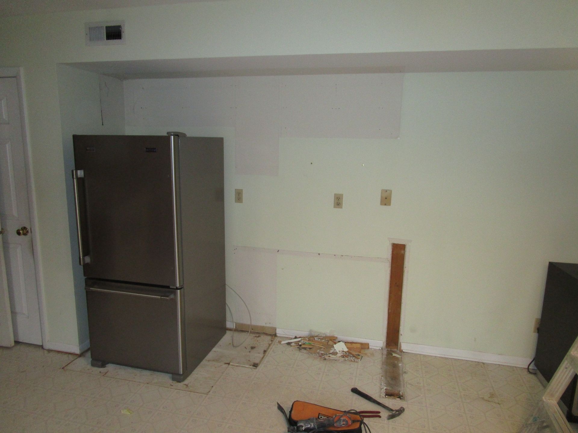 A stainless-steel refrigerator stands in a kitchen undergoing renovations with bare walls and unfinished flooring.