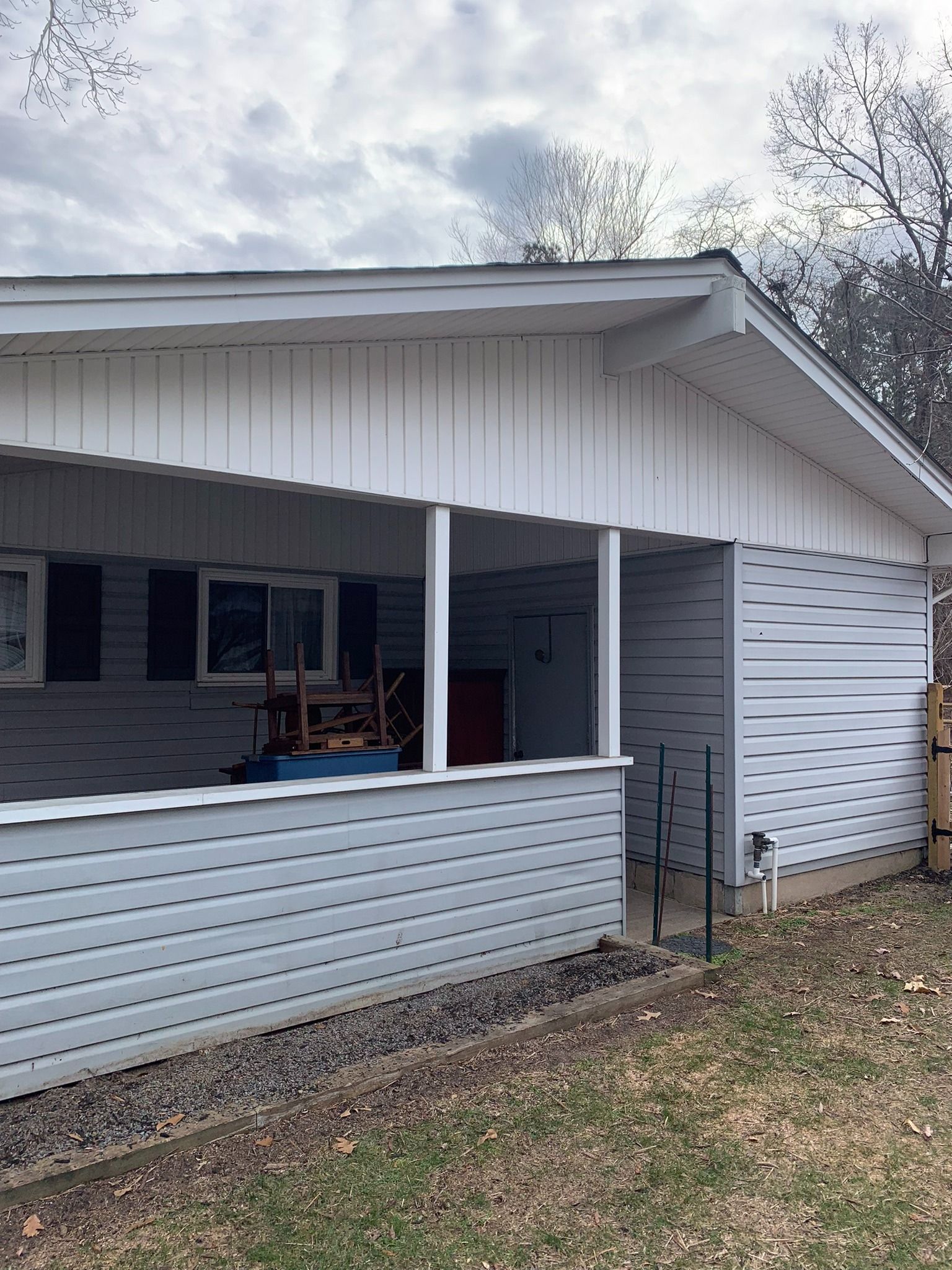 A light gray vinyl-sided house exterior with a covered porch and white vertical wood paneling under the eaves.