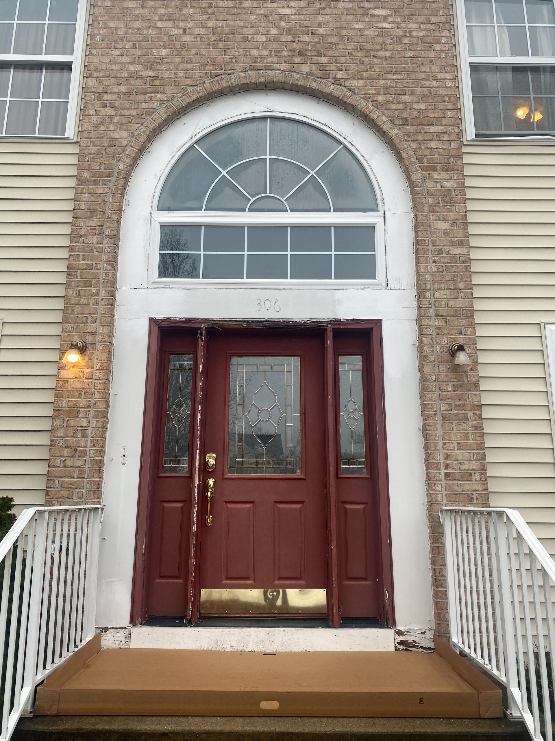 A red front door with side panels, topped by a semicircular window, framed by brick and light-colored siding.