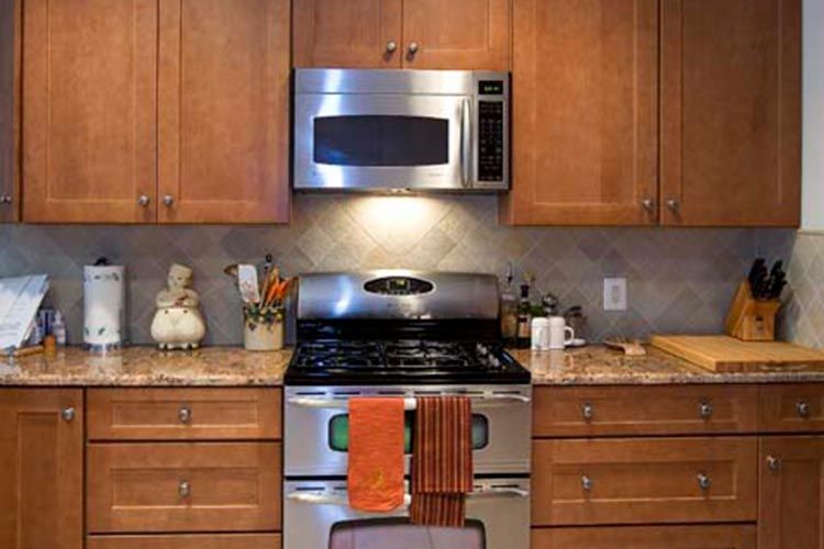 A stainless steel range and microwave set in a kitchen with wooden cabinets and stone countertops.