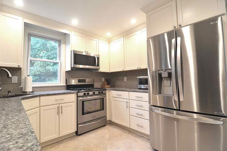 A modern kitchen featuring off-white cabinets, granite countertops, and stainless steel appliances.