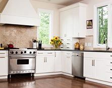 Bright kitchen featuring white cabinets, stainless steel appliances, a range hood, and a vase of sunflowers on the counter.