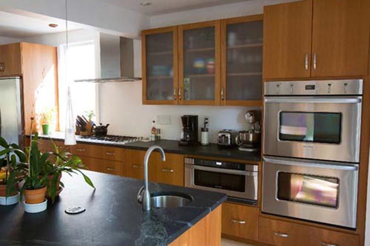 A modern kitchen featuring wooden cabinets, a dark island countertop with a circular sink, and stainless steel appliances.