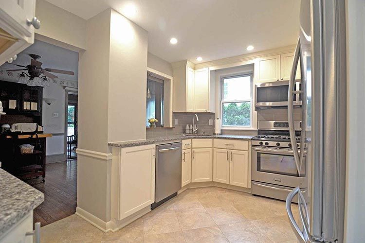 A kitchen with cream cabinets, stainless steel appliances, and a window, viewed from an adjacent room.