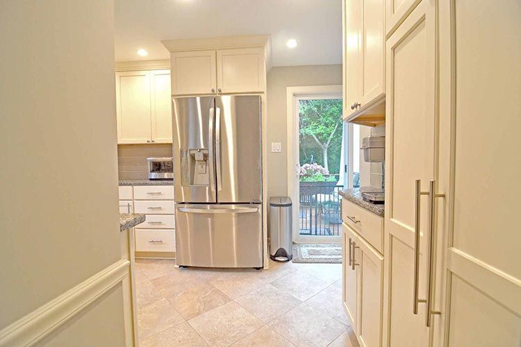 Modern kitchen with cream cabinets, stainless steel refrigerator, tile floors, and a door opening to a patio.