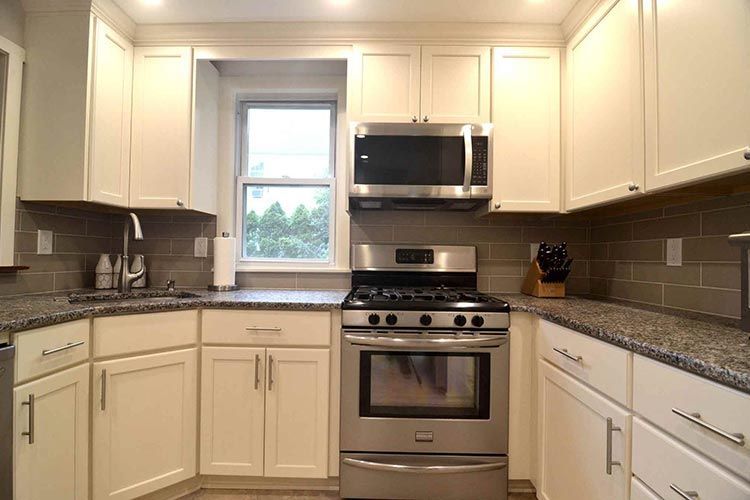 A modern kitchen with white cabinets, stainless steel appliances, speckled granite countertops, and a subway tile backsplash.