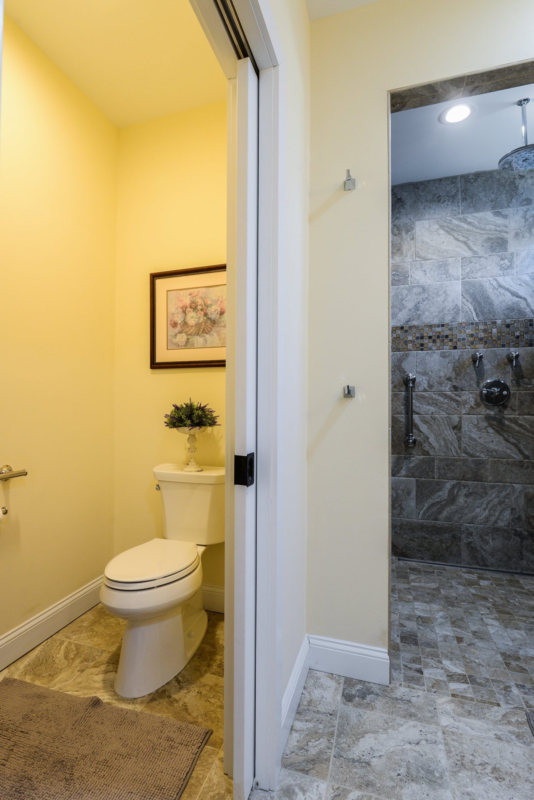 A bathroom with a toilet in a small nook, beige walls, and a walk-in shower with grey tiled walls and floor.