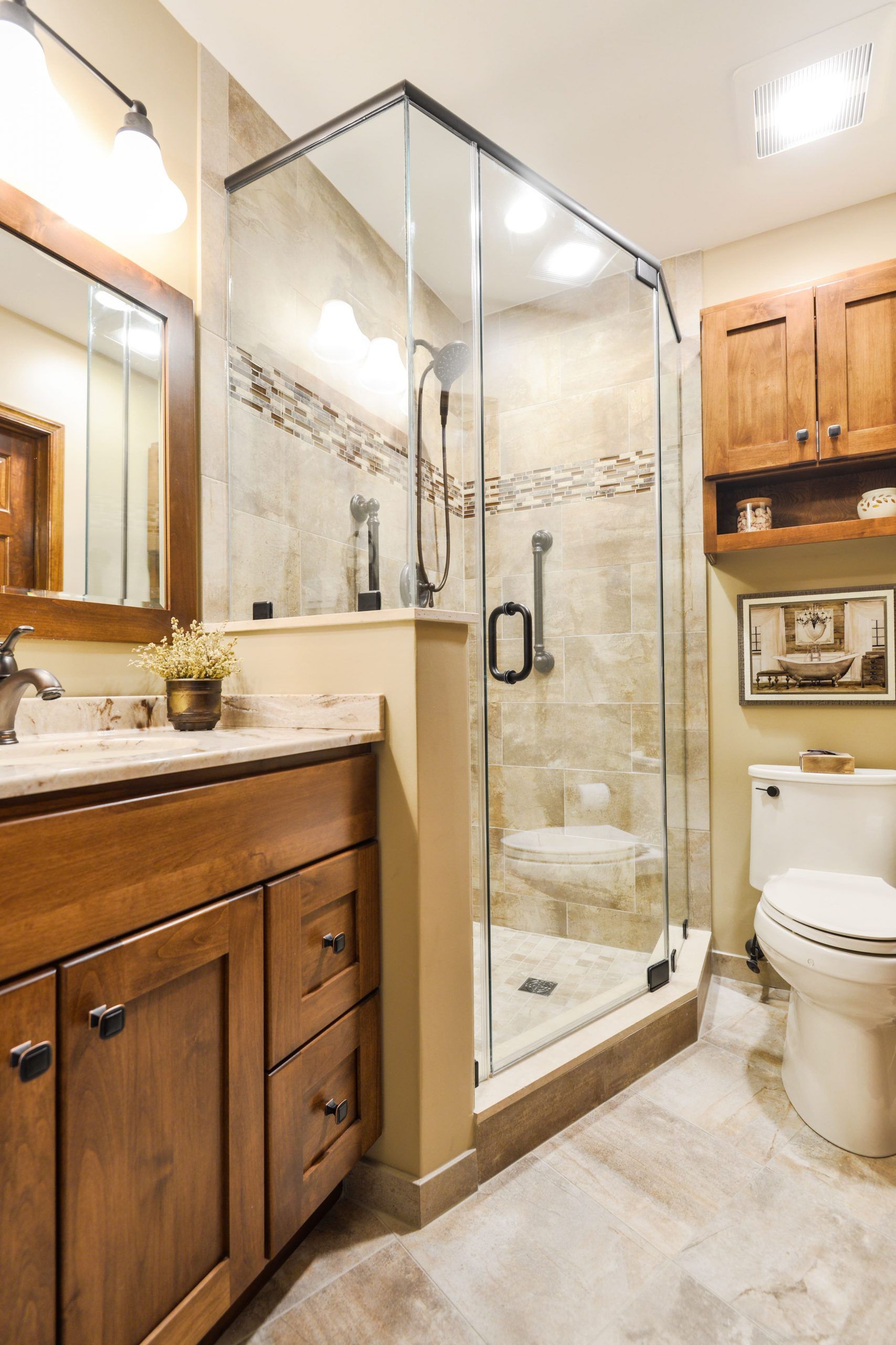 A bathroom with a wooden vanity, a glass-enclosed corner shower with beige tiles, and a white toilet.