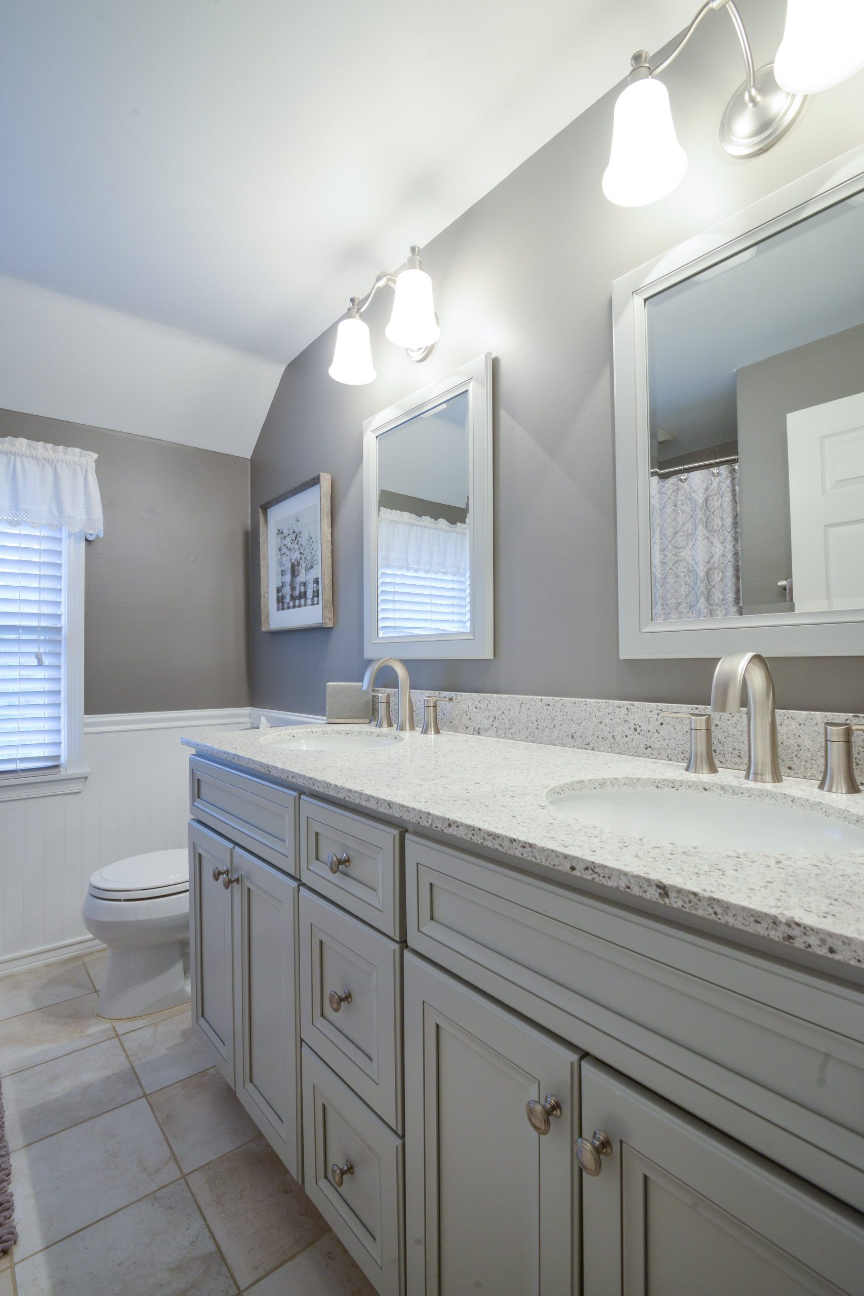 A modern bathroom vanity with a speckled countertop, dual sinks, and two mirrors on a gray wall.