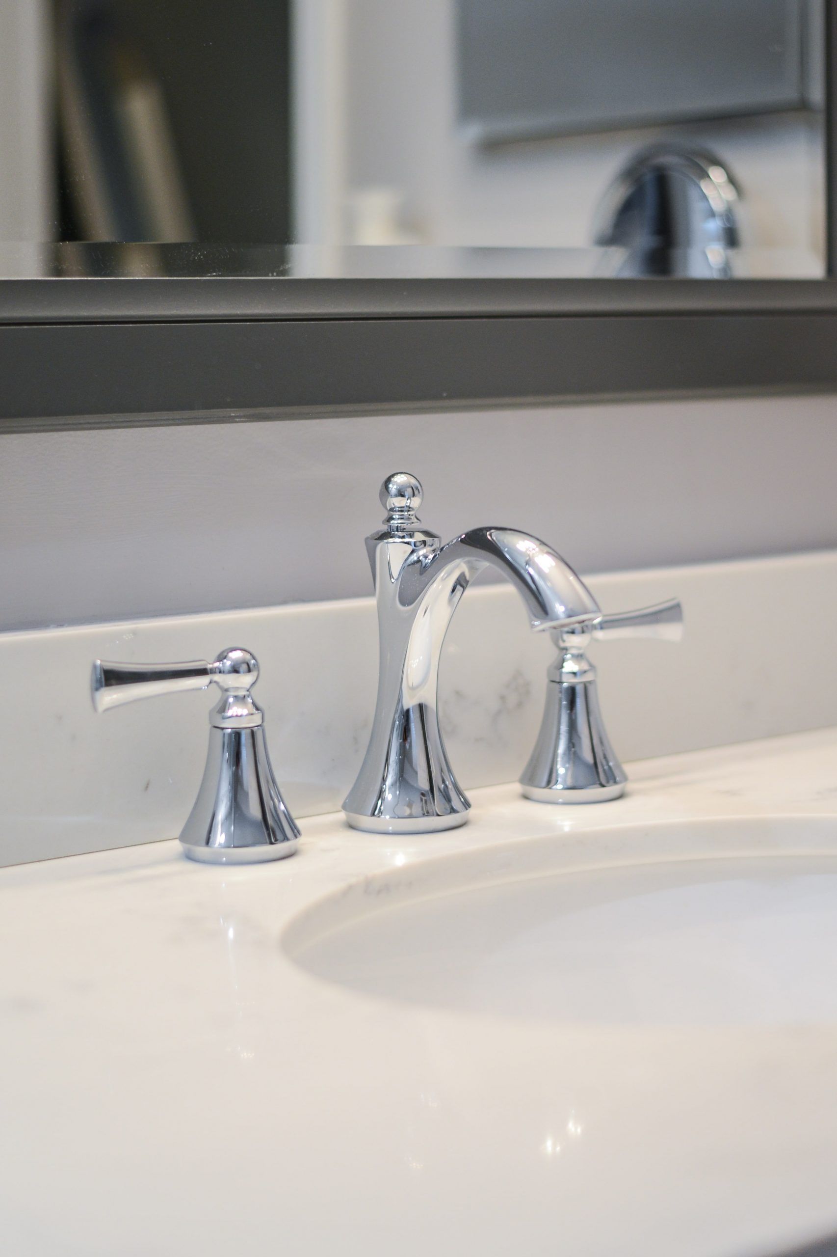 A polished chrome bathroom faucet with two lever handles mounted on a white countertop below a mirror.