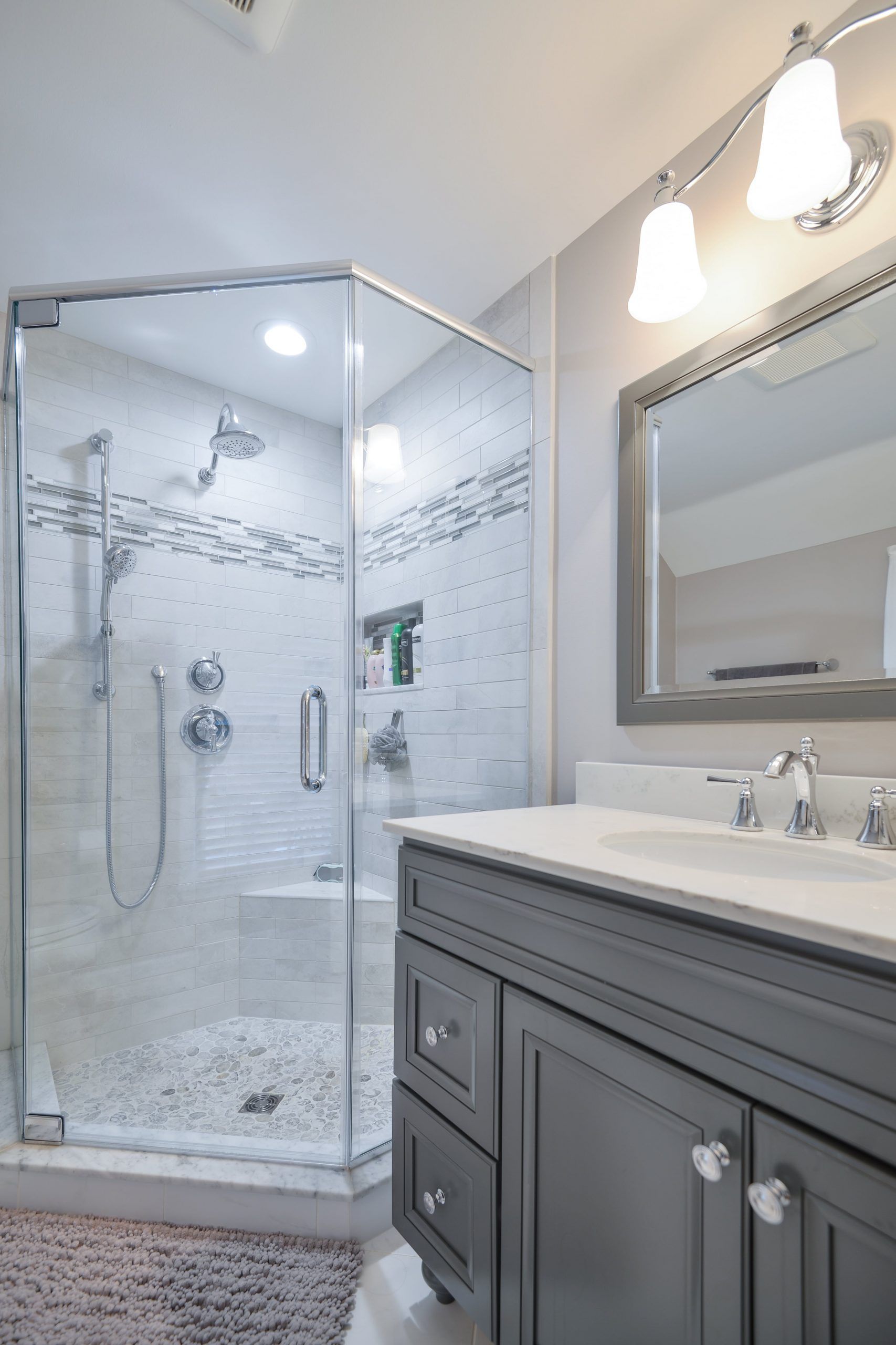 A modern bathroom featuring a corner glass shower with pebble floor and a dark gray vanity with a framed mirror.