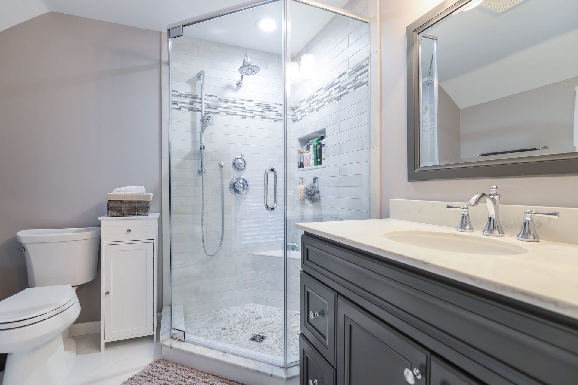 A modern bathroom with a glass-enclosed shower, dark gray vanity, white toilet, and a large mirror.