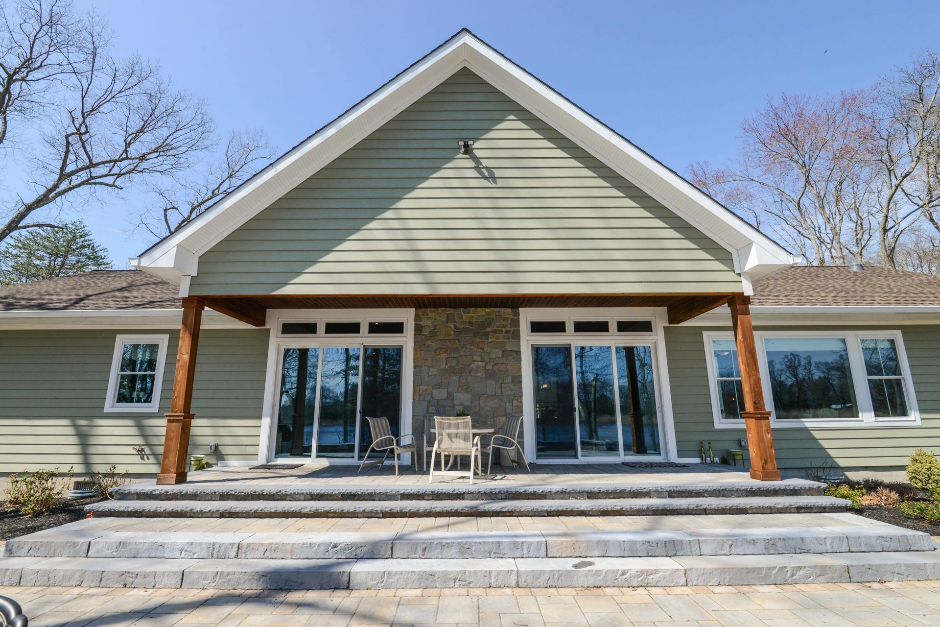 A light green house with a gabled roof, two sliding glass doors, a stone fireplace, and a tiered stone patio.