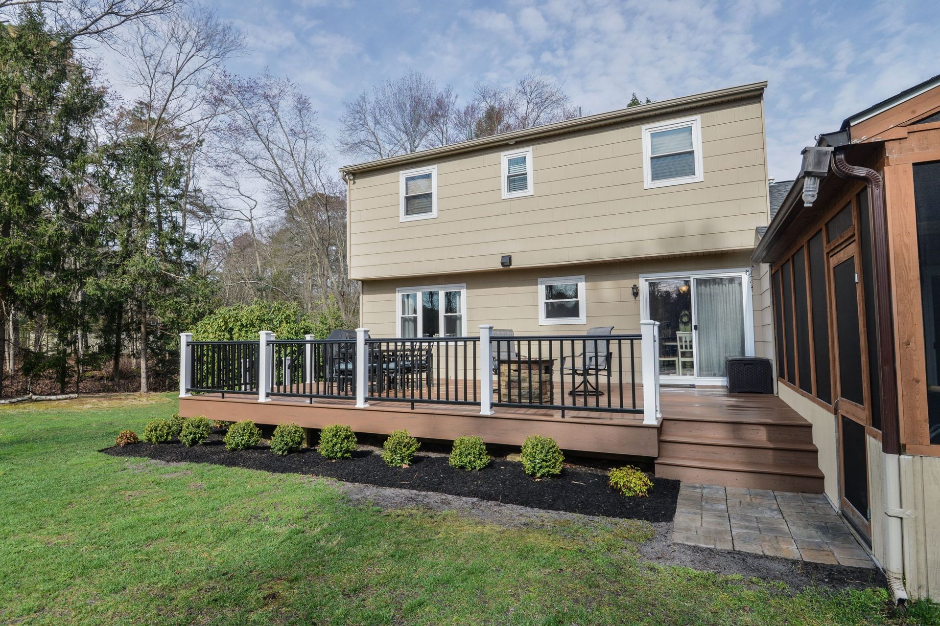 A beige two-story house features a spacious brown wooden deck with black railings and a matching staircase leading down.
