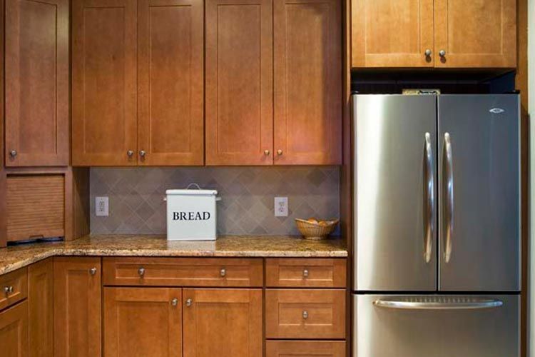 A kitchen with medium-toned wooden cabinets, granite countertops, a stainless steel refrigerator, and a bread bin.