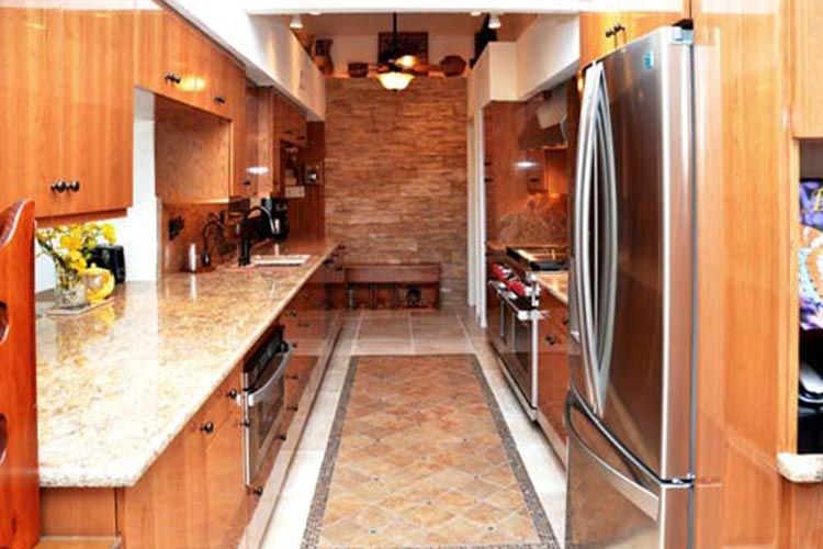 A galley-style kitchen featuring wood cabinets, granite countertops, stainless steel appliances, and a stone accent wall.
