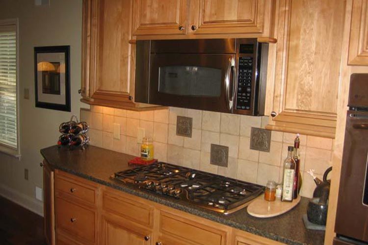 A kitchen stovetop set into a dark countertop beneath a stainless steel microwave and light wood cabinets.