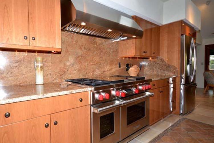 A kitchen with light wood cabinets, granite countertops, a large stainless steel range, and a matching range hood.