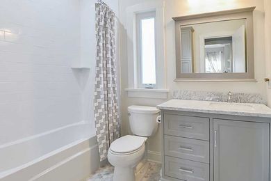 A bright, modern bathroom with a white bathtub, a grey vanity with a mirror, a window, and a white toilet.