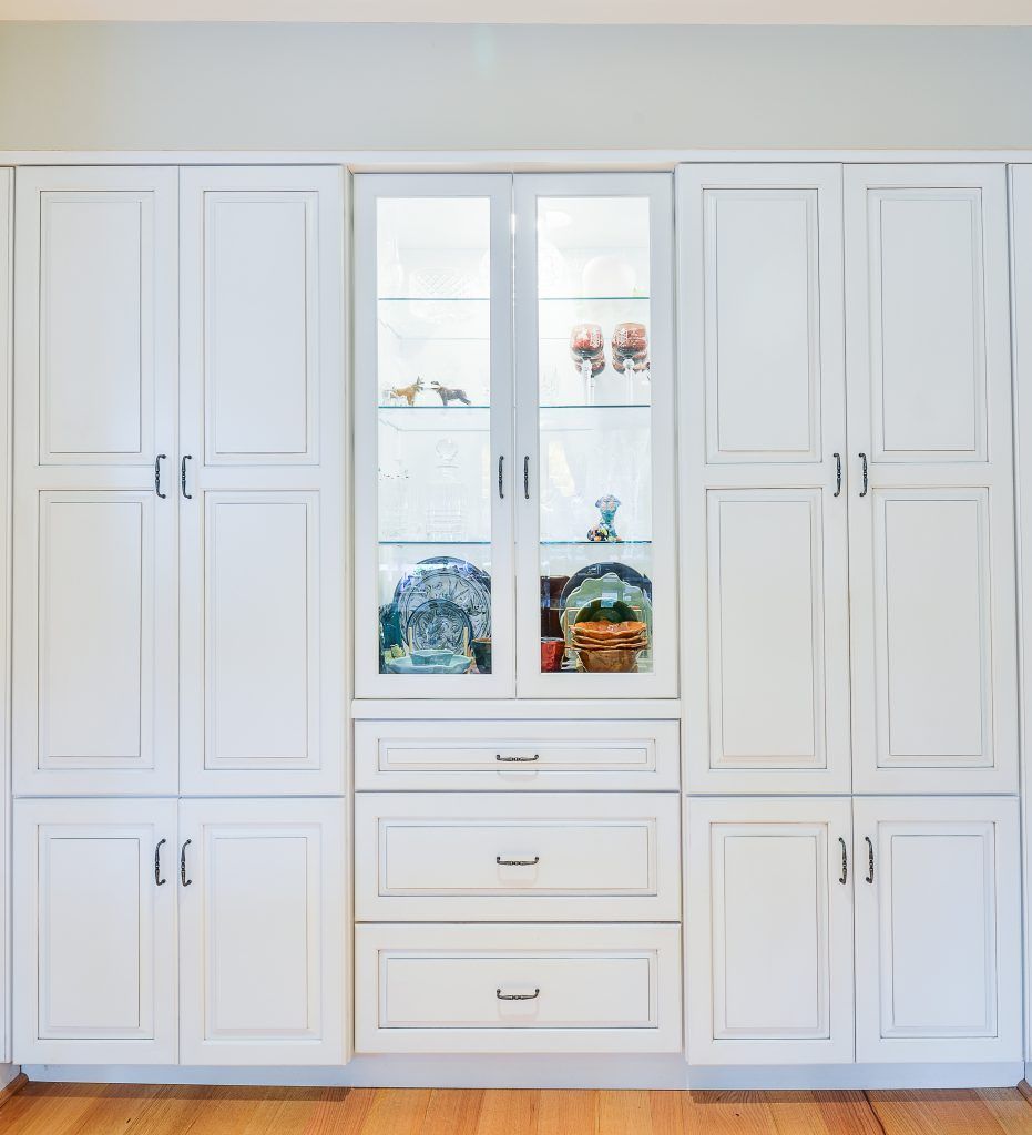 A wall of white cabinetry with two side storage units, a central glass-front display case, and three bottom drawers.