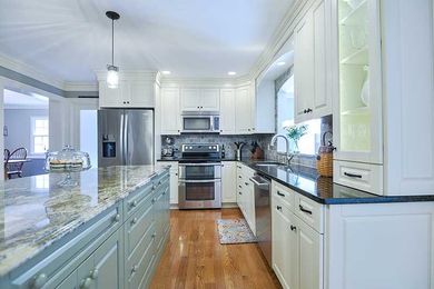 A bright, modern kitchen features white cabinetry, a light blue island with granite countertops, and stainless appliances.