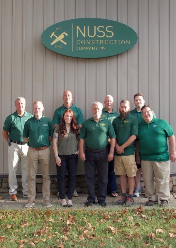 A group of eleven people in green shirts stand in front of a sign for the Nuss Construction Company.
