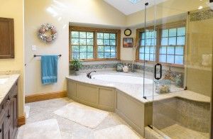 A bright bathroom featuring a large corner bathtub, a glass-enclosed shower, and a light blue towel hanging on the wall.