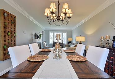 A formal dining room featuring a dark wood table with six white chairs, a decorative centerpiece, and a chandelier above.