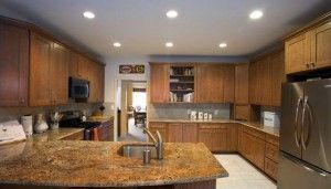 A bright kitchen with wooden cabinets, granite countertops, a central island with a sink, and stainless steel appliances.
