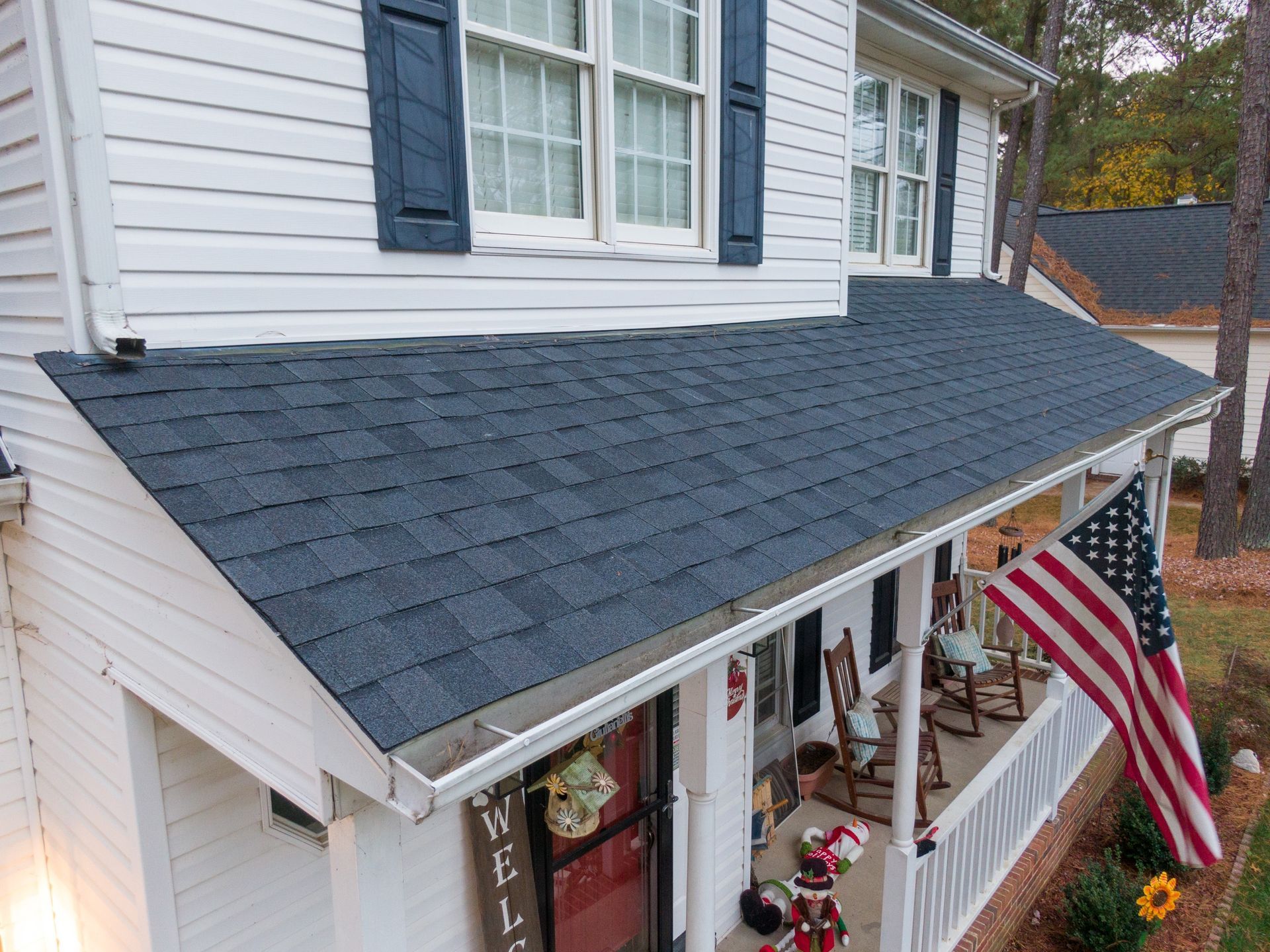 Decorated front porch with American flag and Halloween decorations under a gray shingled awning