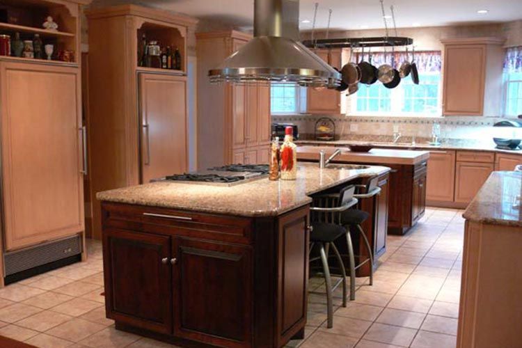 Spacious kitchen with wood cabinets, granite-topped islands, a stainless steel range hood, and tile flooring.