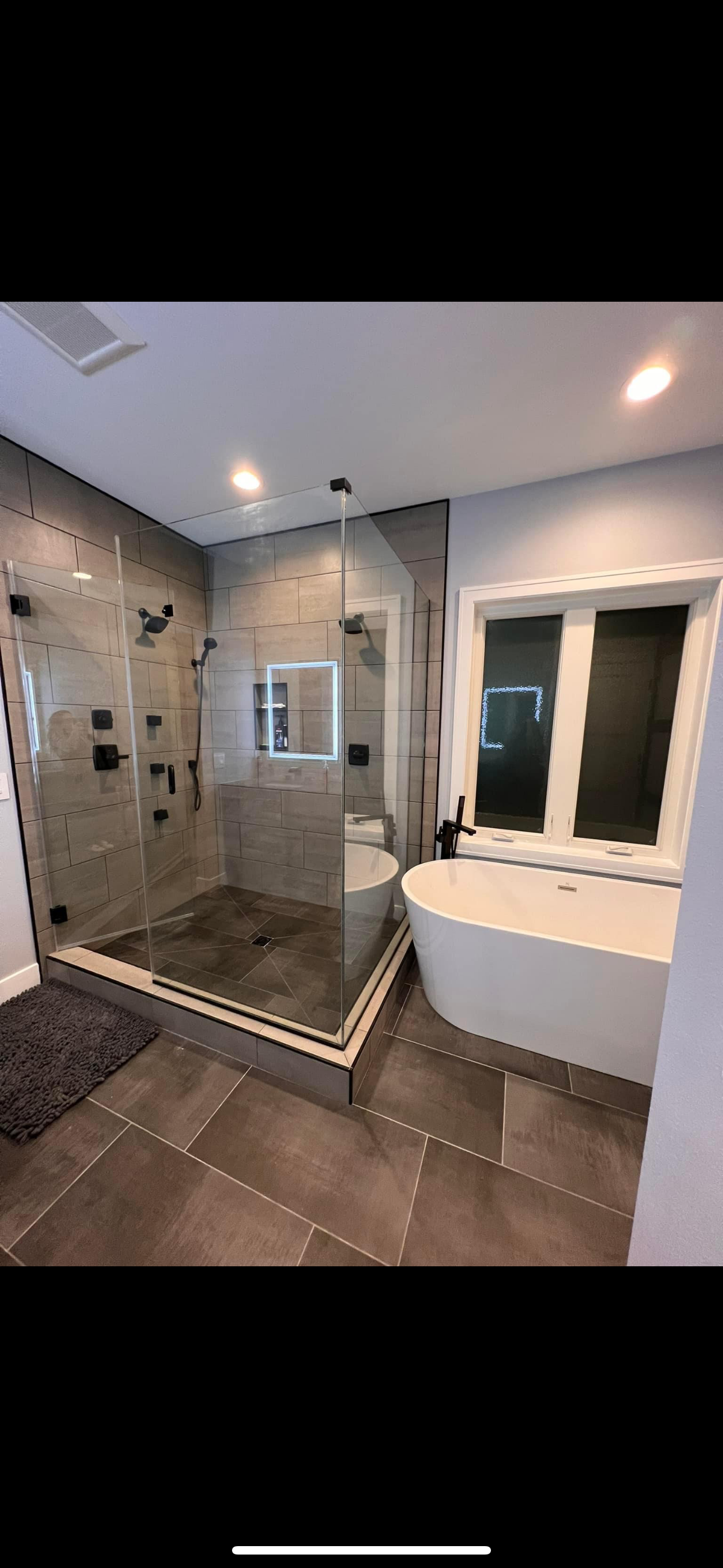 Modern bathroom with a walk-in shower, a freestanding bathtub, and large window.
