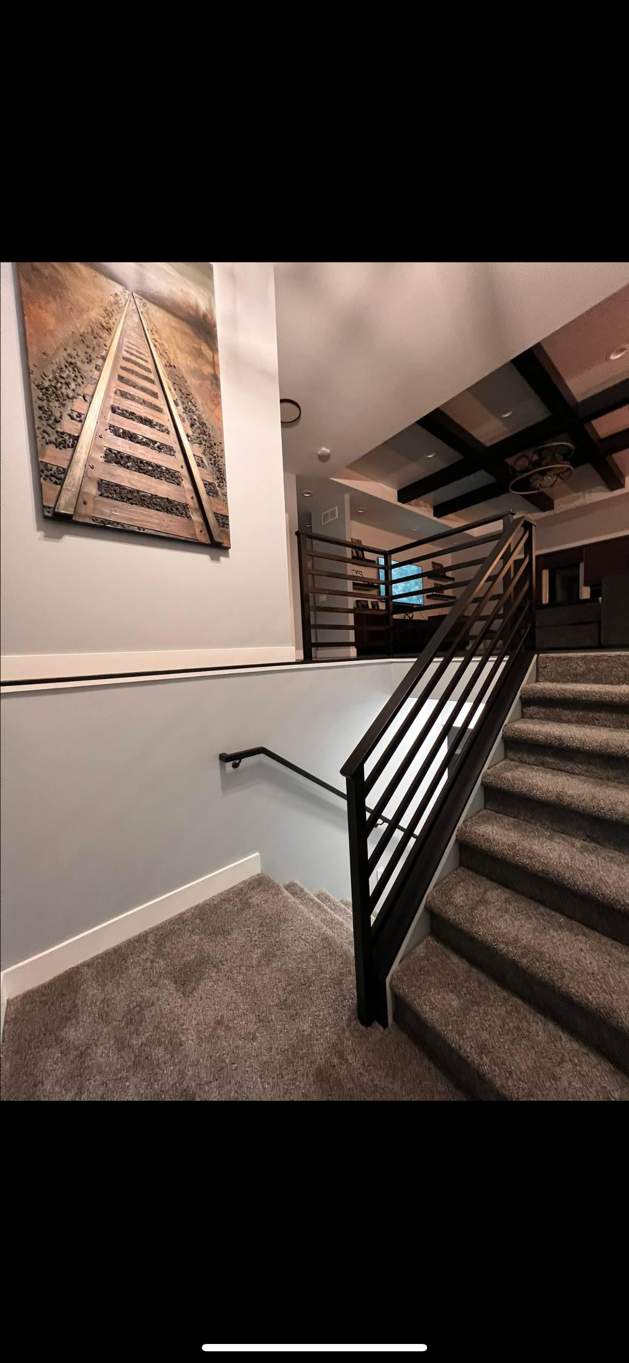 A staircase with black railing and gray carpet. A railway art decor is hanging on the wall.